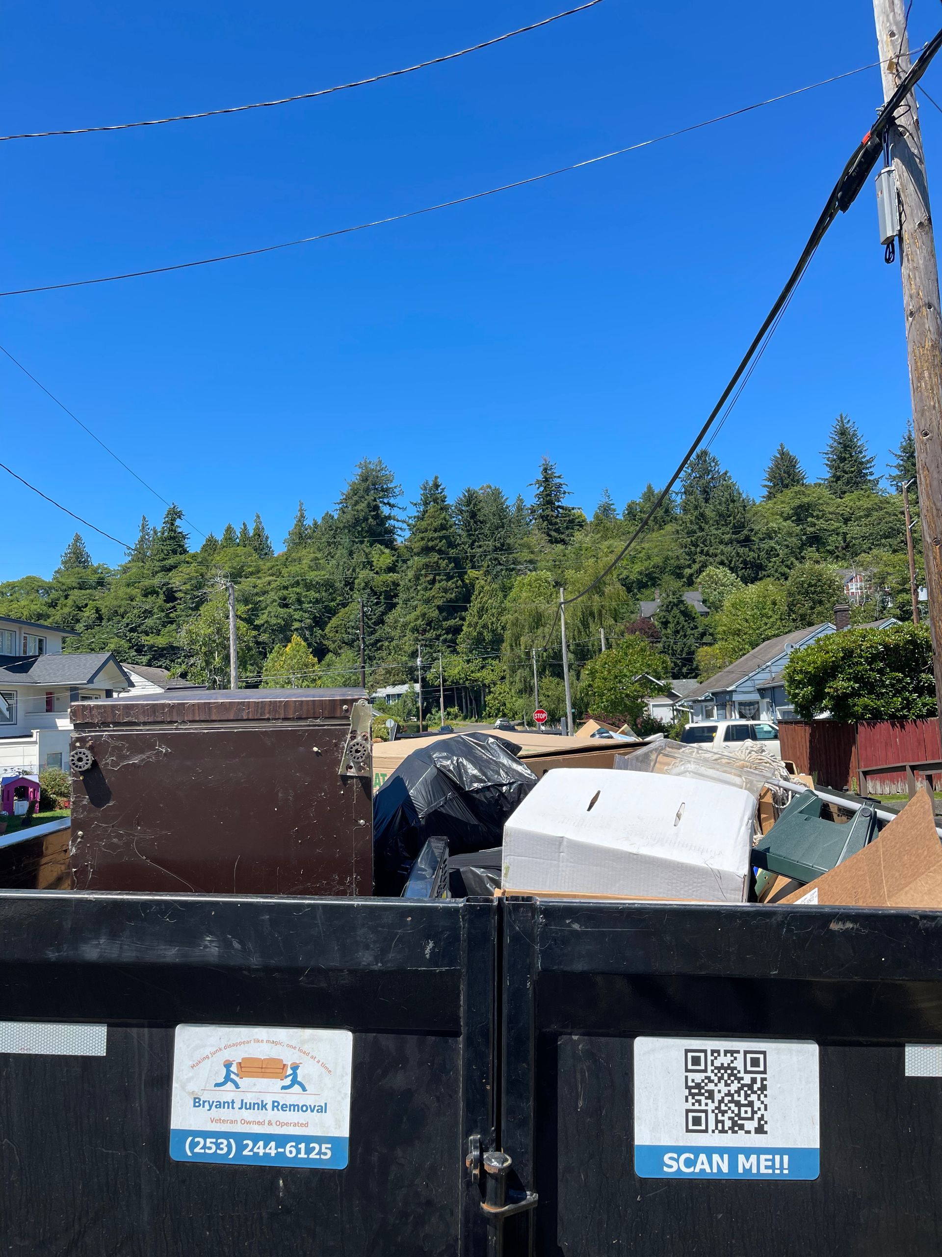 Dumpster filled with debris, against a backdrop of trees and blue sky.