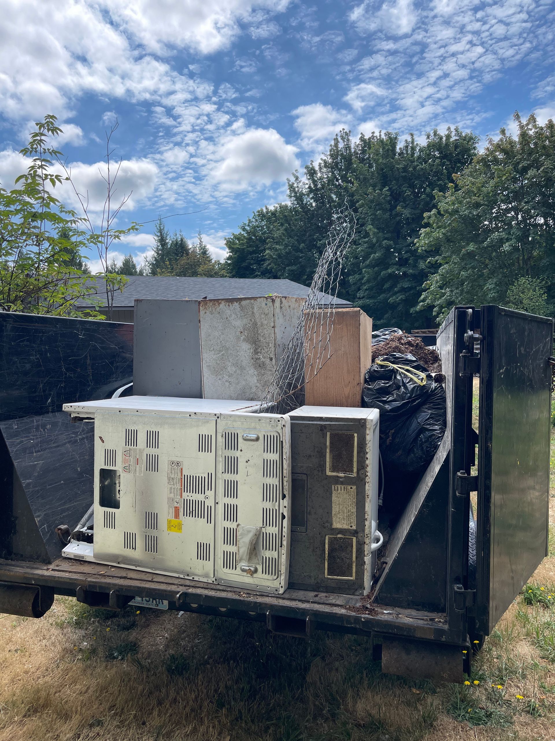 Dumpster overflowing with debris, including a white crate, insulation, and other discarded items outdoors.