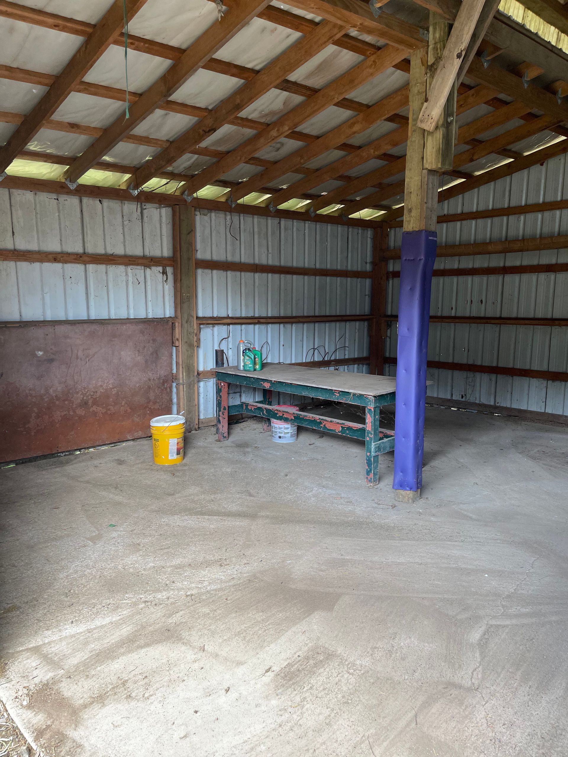 Inside of a barn with a work bench, tools, and a dirt floor.