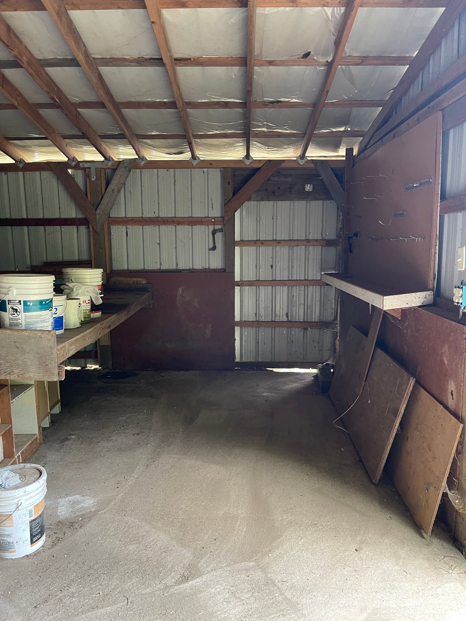 Interior of a wooden shed. Corrugated metal walls, work benches, and various supplies are visible.