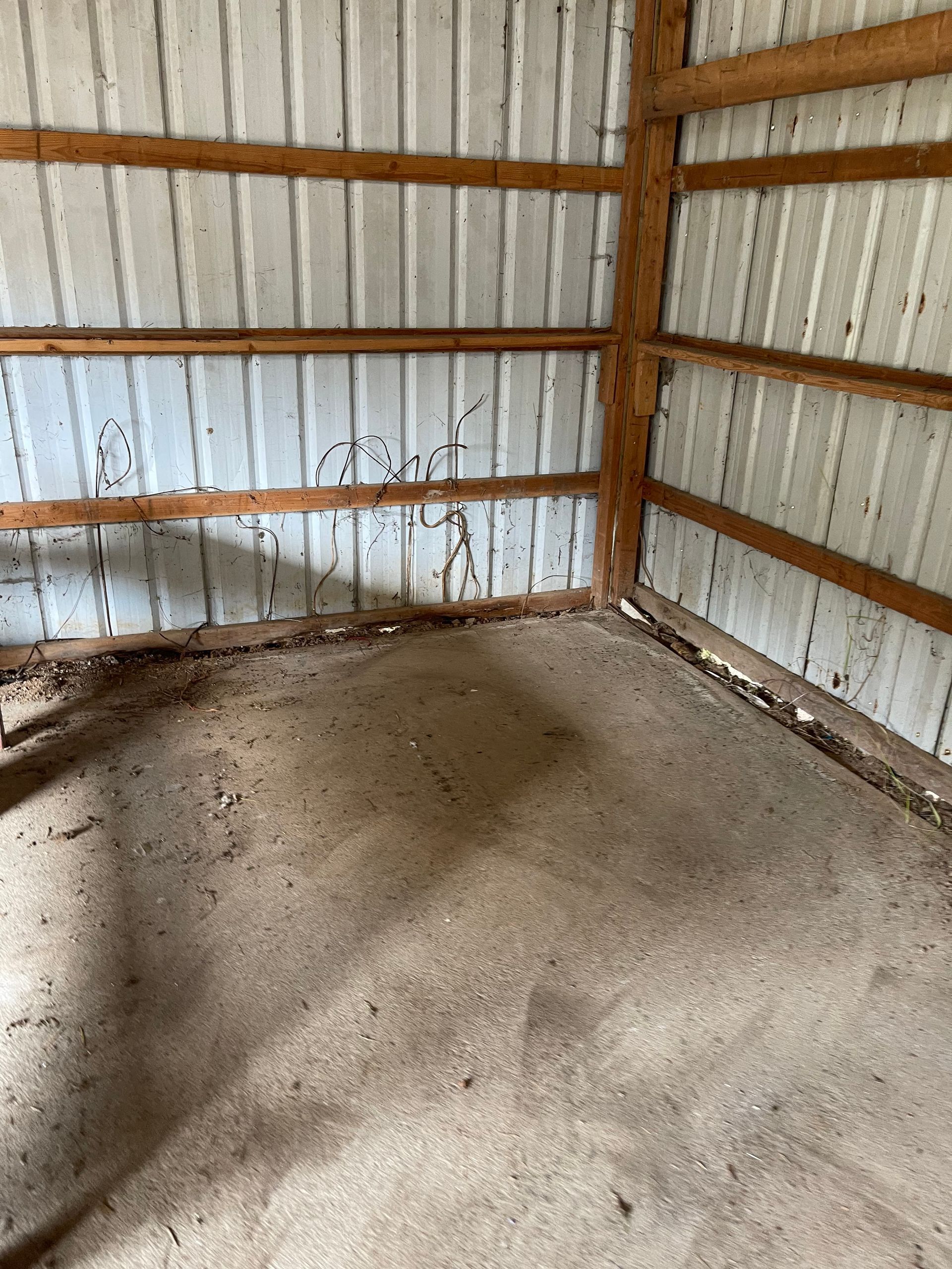 Interior of a weathered metal-walled shed with a dirt floor and wooden support beams.