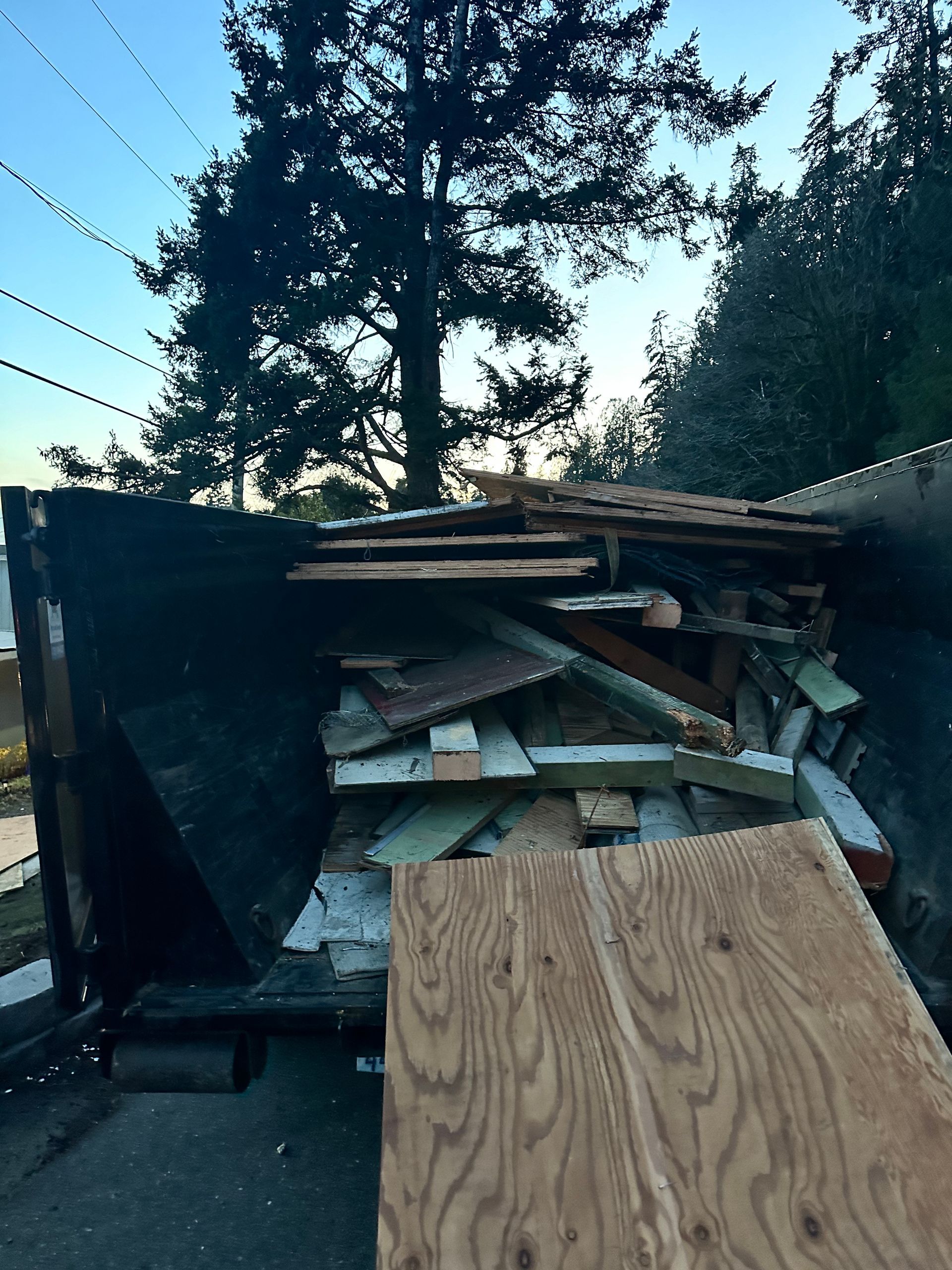 Dumpster filled with construction debris, including wood planks and boards, outdoors.
