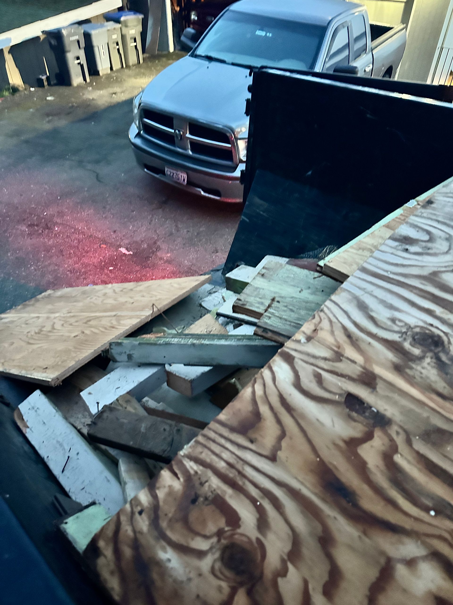 A truck bed filled with wood scraps; a silver Dodge truck and trash cans are visible.