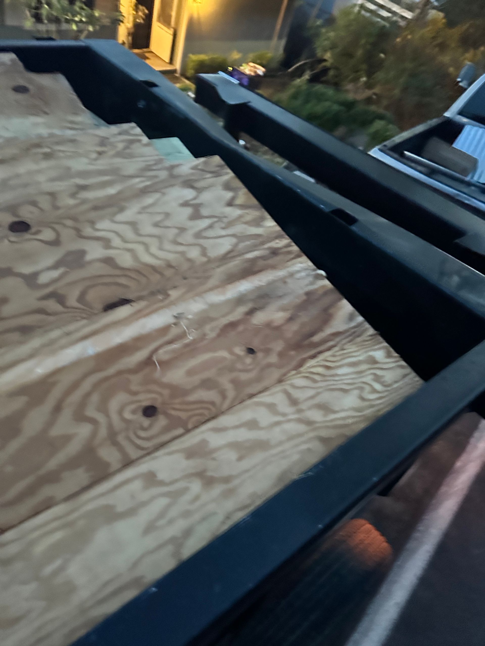 Plywood deck with black metal supports, viewed from above, outdoors.