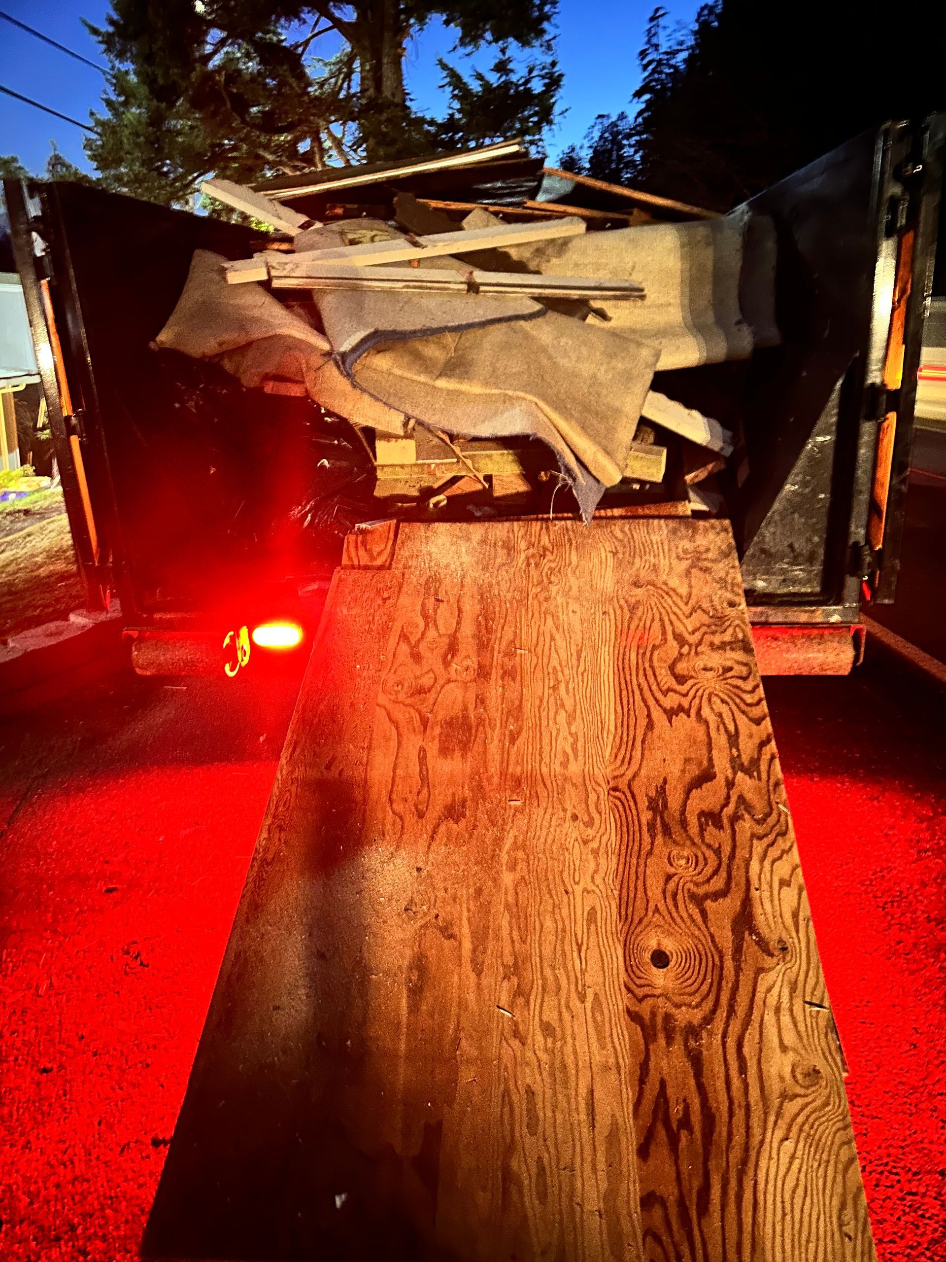 Ramp leading to a dumpster filled with construction debris, illuminated by a red light in a nighttime setting.