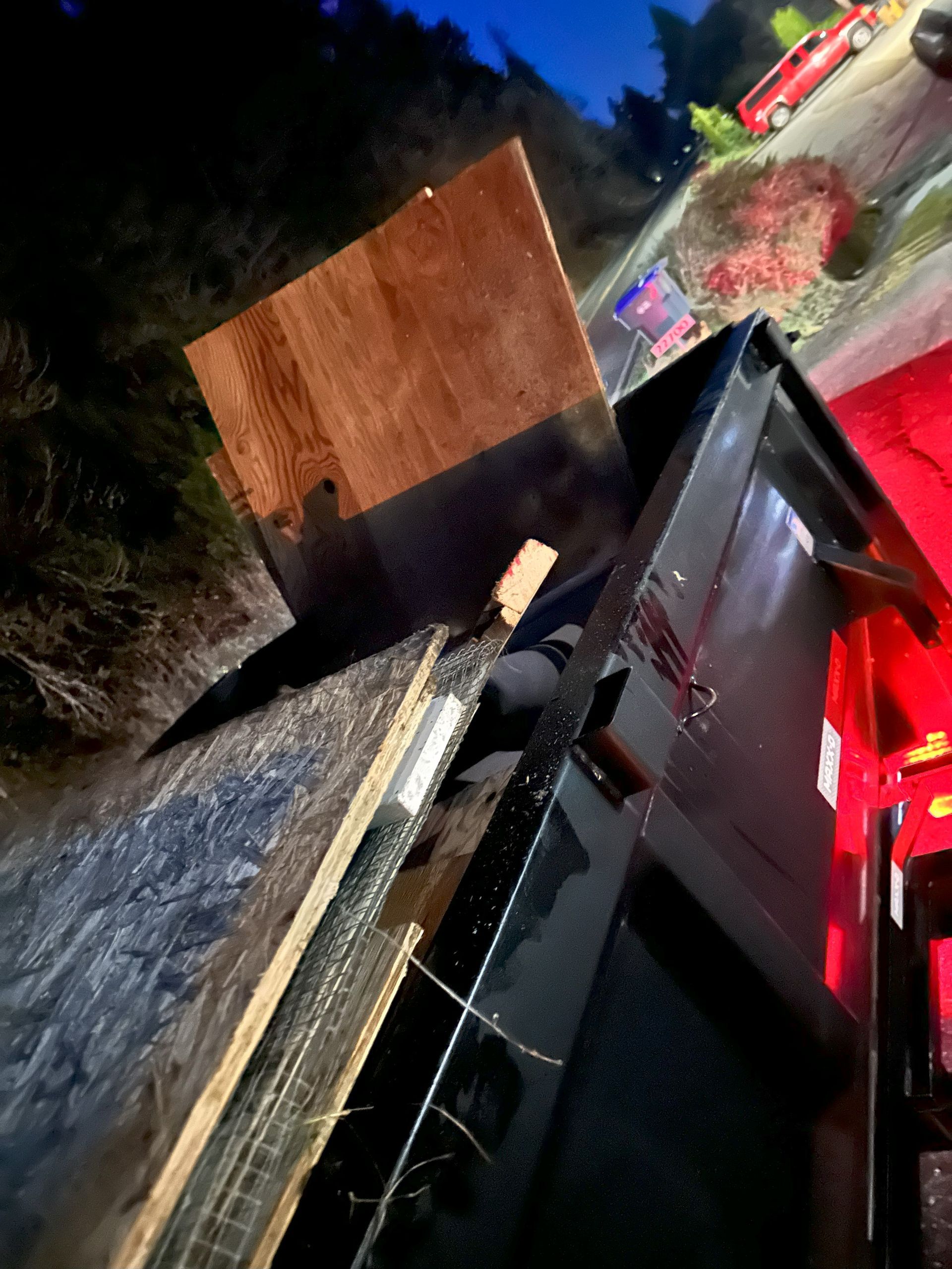 Overturned dark truck with a wooden panel on the side of a road at night; emergency vehicle lights visible.