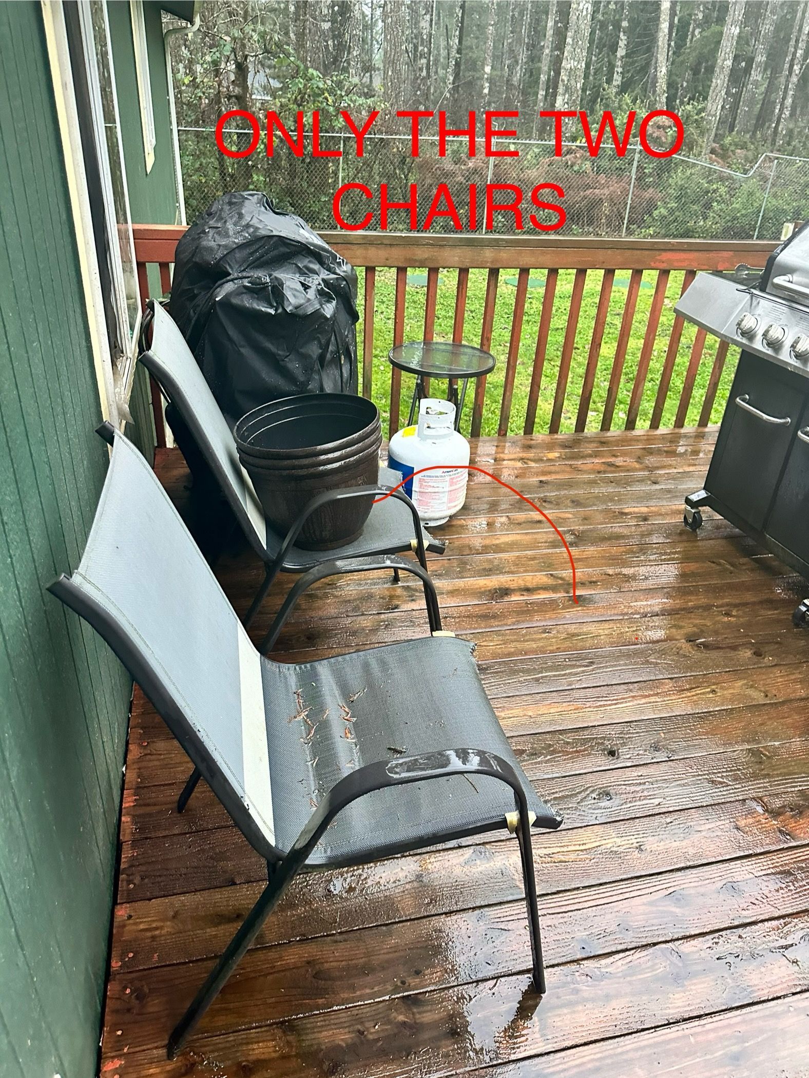 Two metal chairs on a wet wooden deck next to a grill and propane tank.