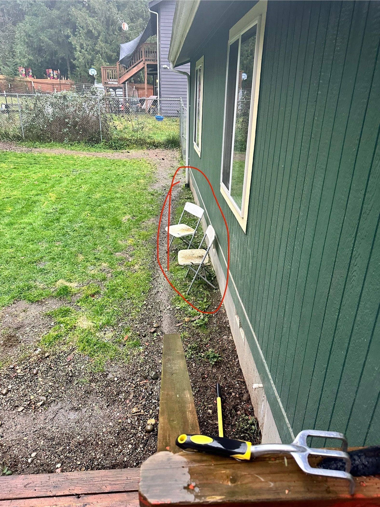 A green house with a flooded yard. A hose and steps are in the foreground.