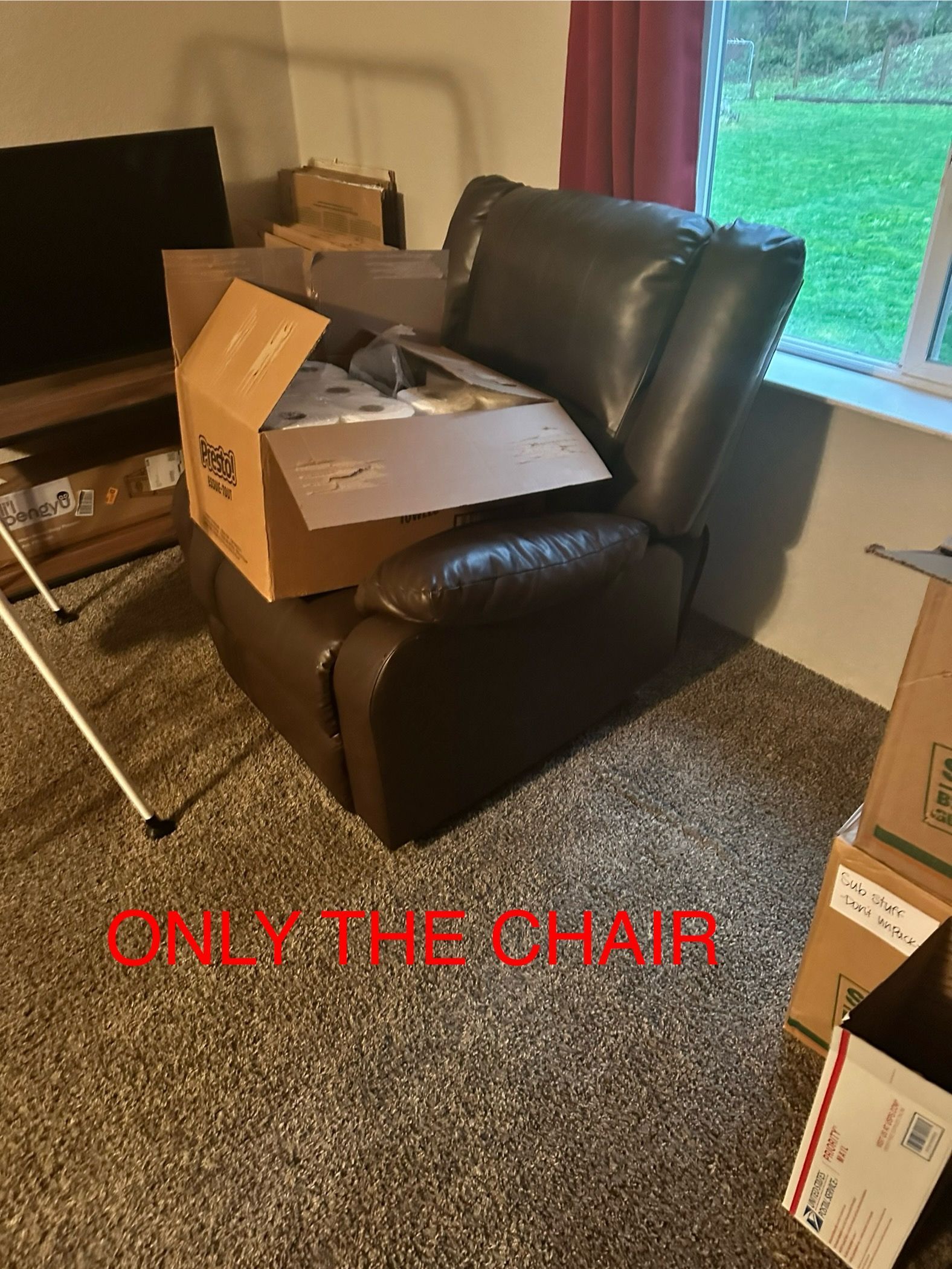 Brown leather recliner with cardboard boxes in a room with carpet and a window.