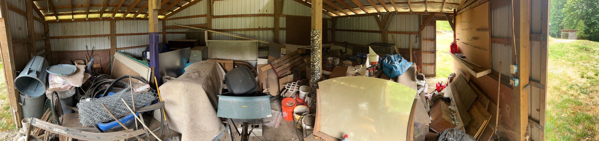 A cluttered shed interior with various items piled up; a doorway leads outside.