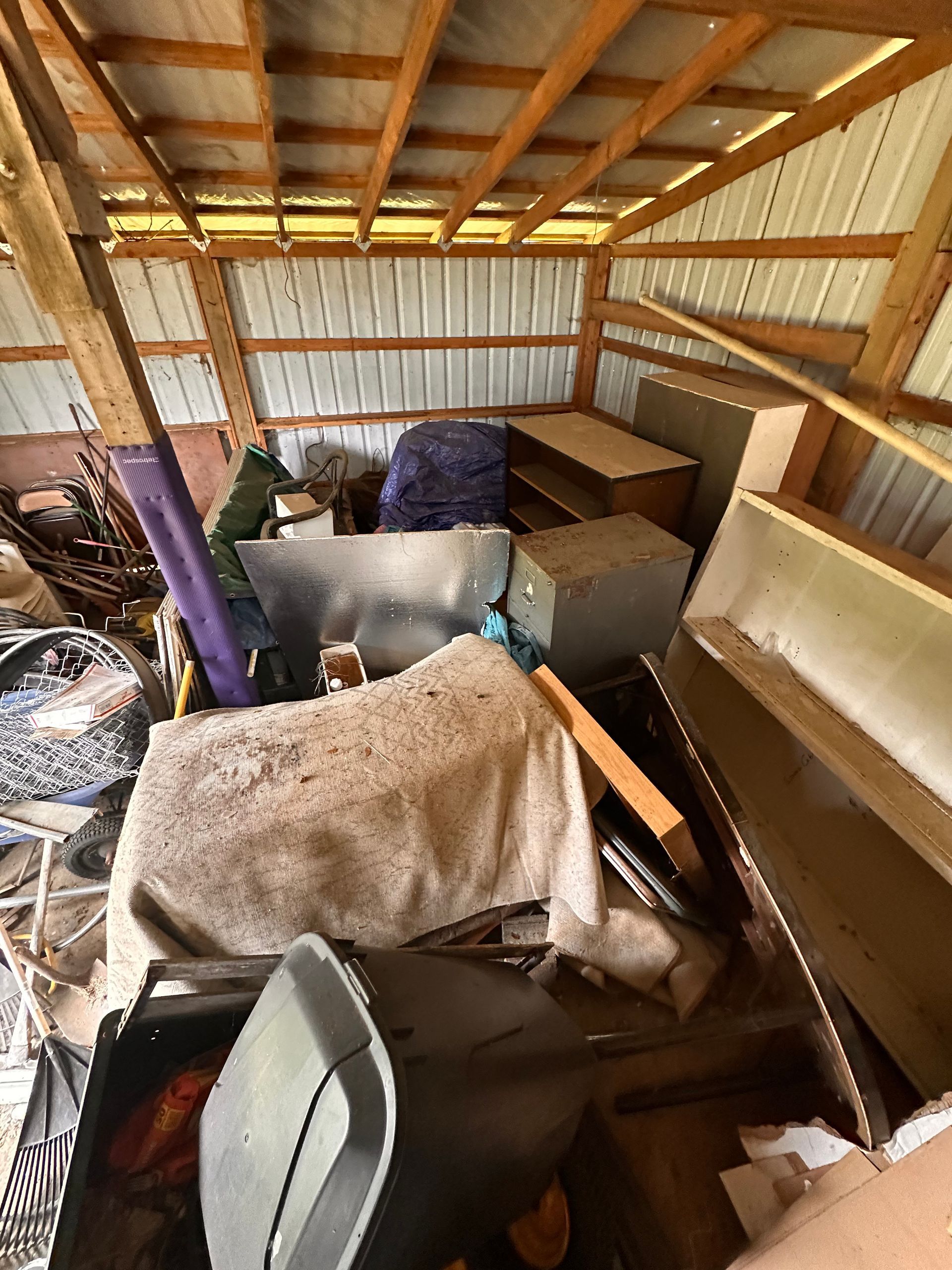 Cluttered shed interior with furniture, trash, and debris, appearing messy and disorganized.