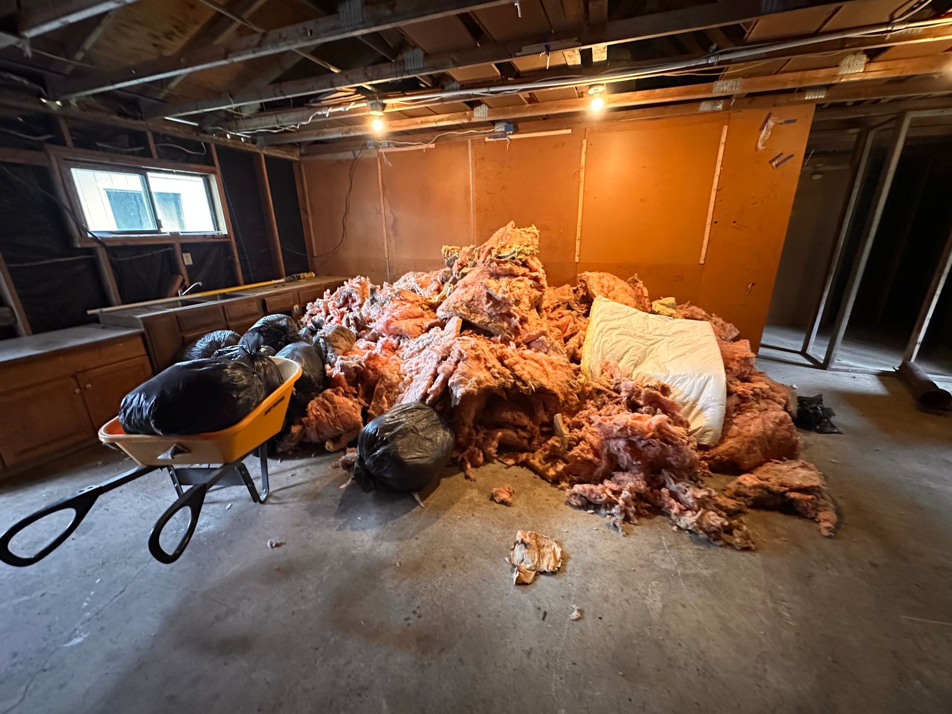 Pile of pink insulation and black bags of debris in a basement undergoing renovation.