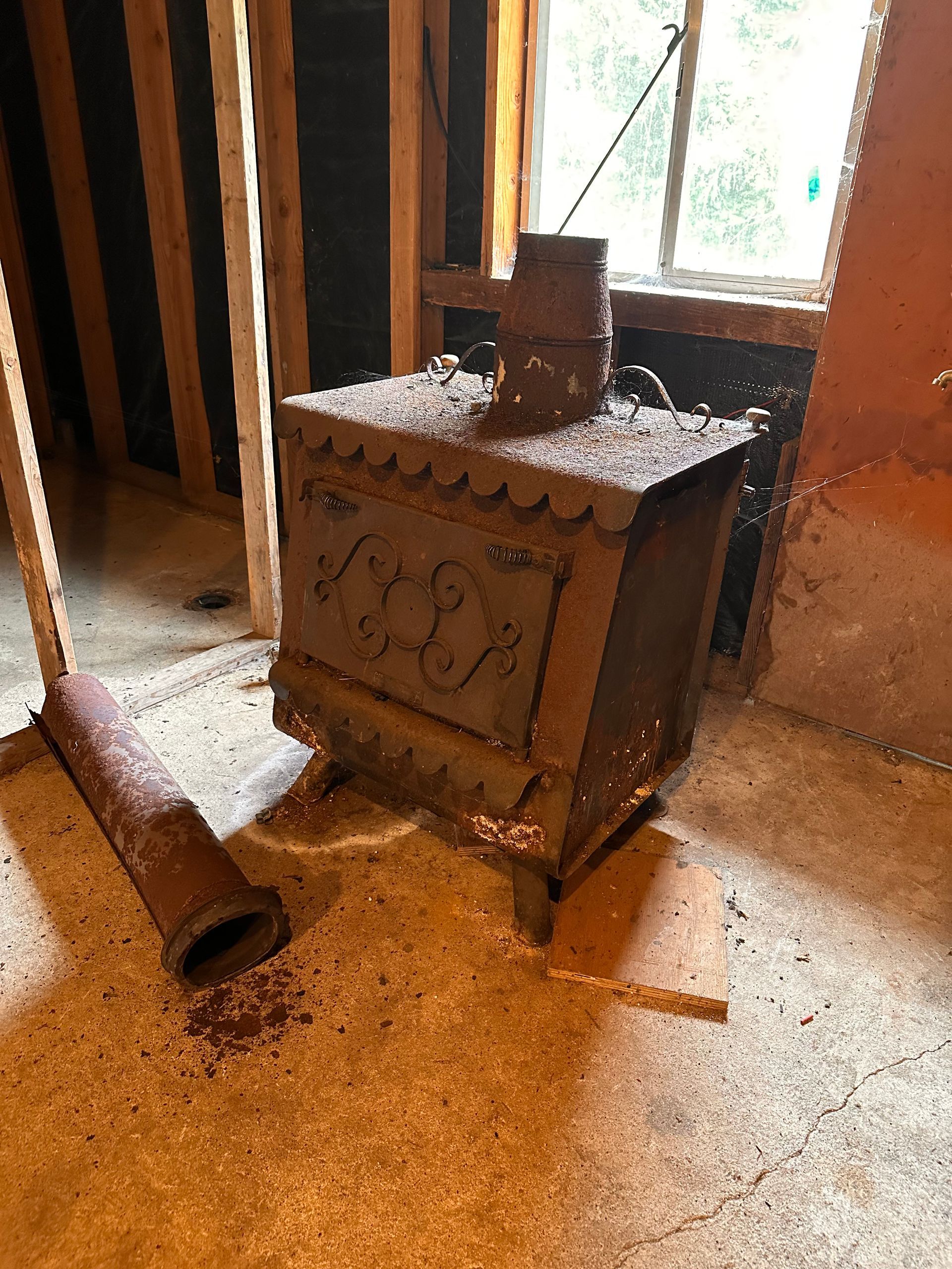 Rusty, antique wood-burning stove with decorative scrollwork, in a dusty basement.