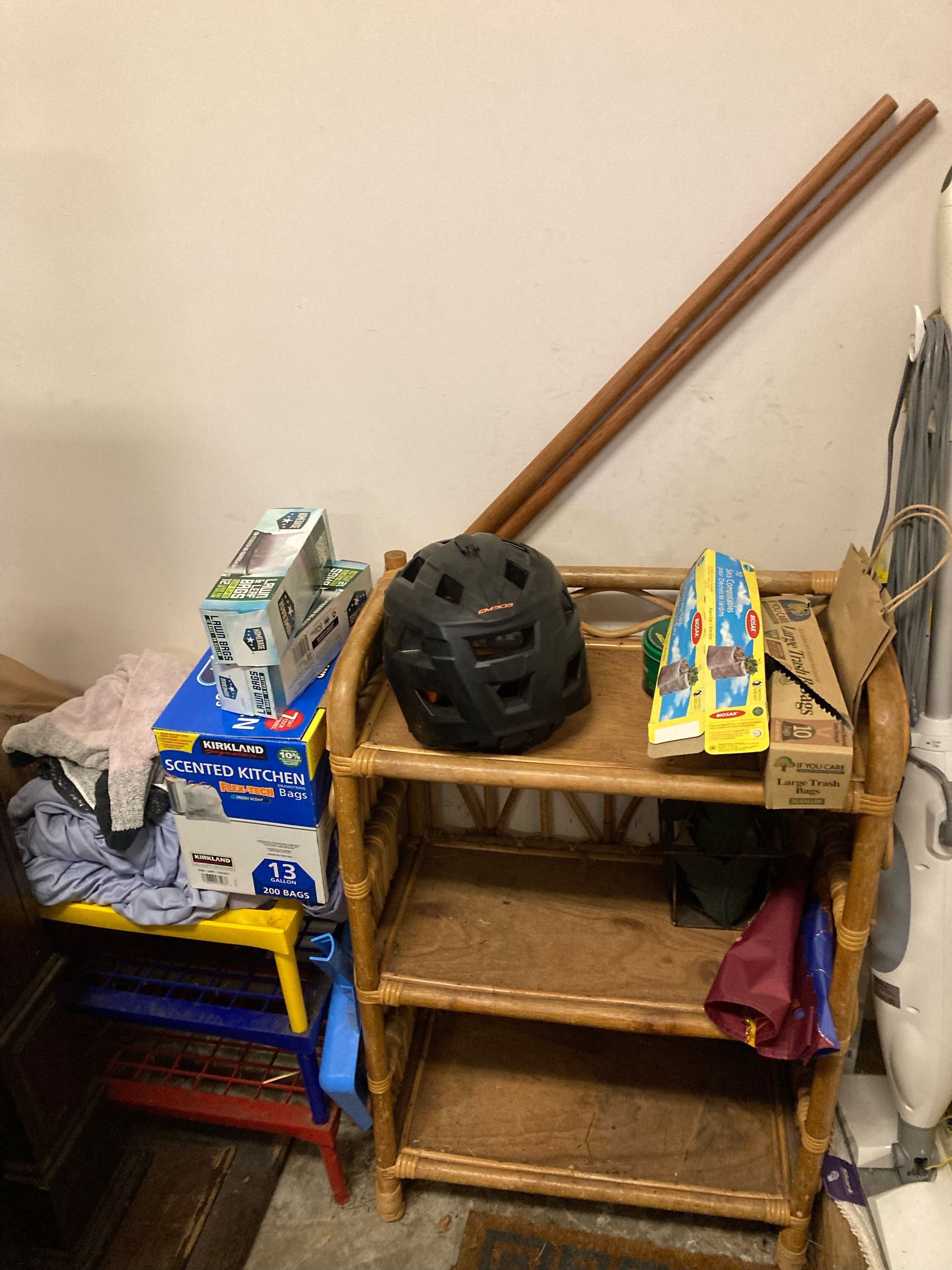 A cluttered storage area with a shelf holding a helmet, boxes, and leaning wooden poles.