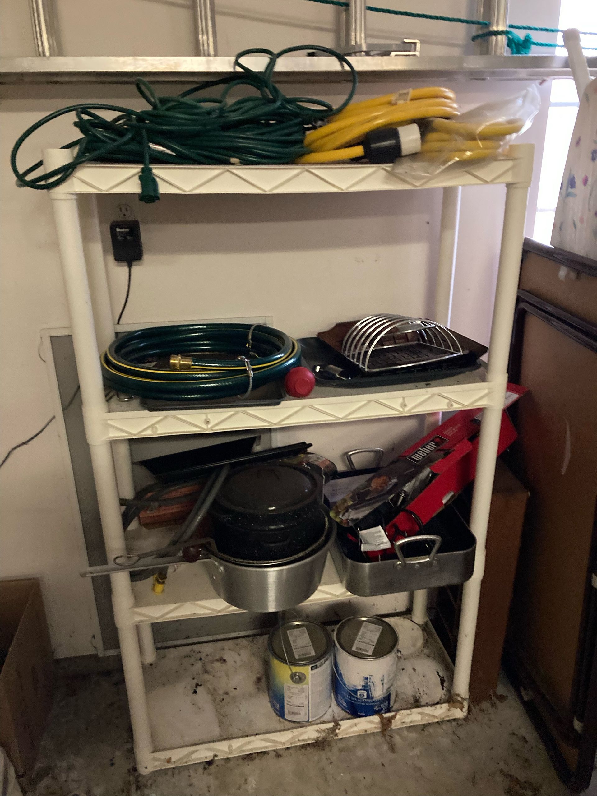 White shelving unit holding tools, paint cans, and garden hoses in a garage.