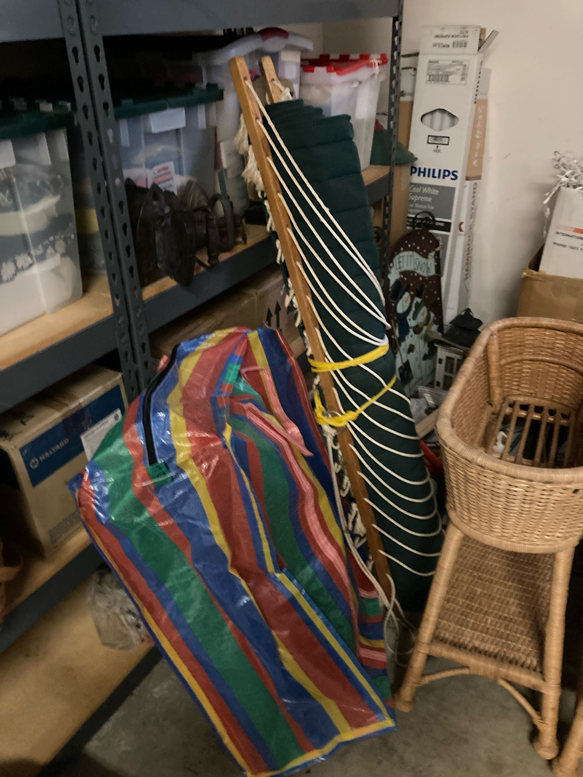 A cluttered storage area with an umbrella, wicker chair, and storage bins.