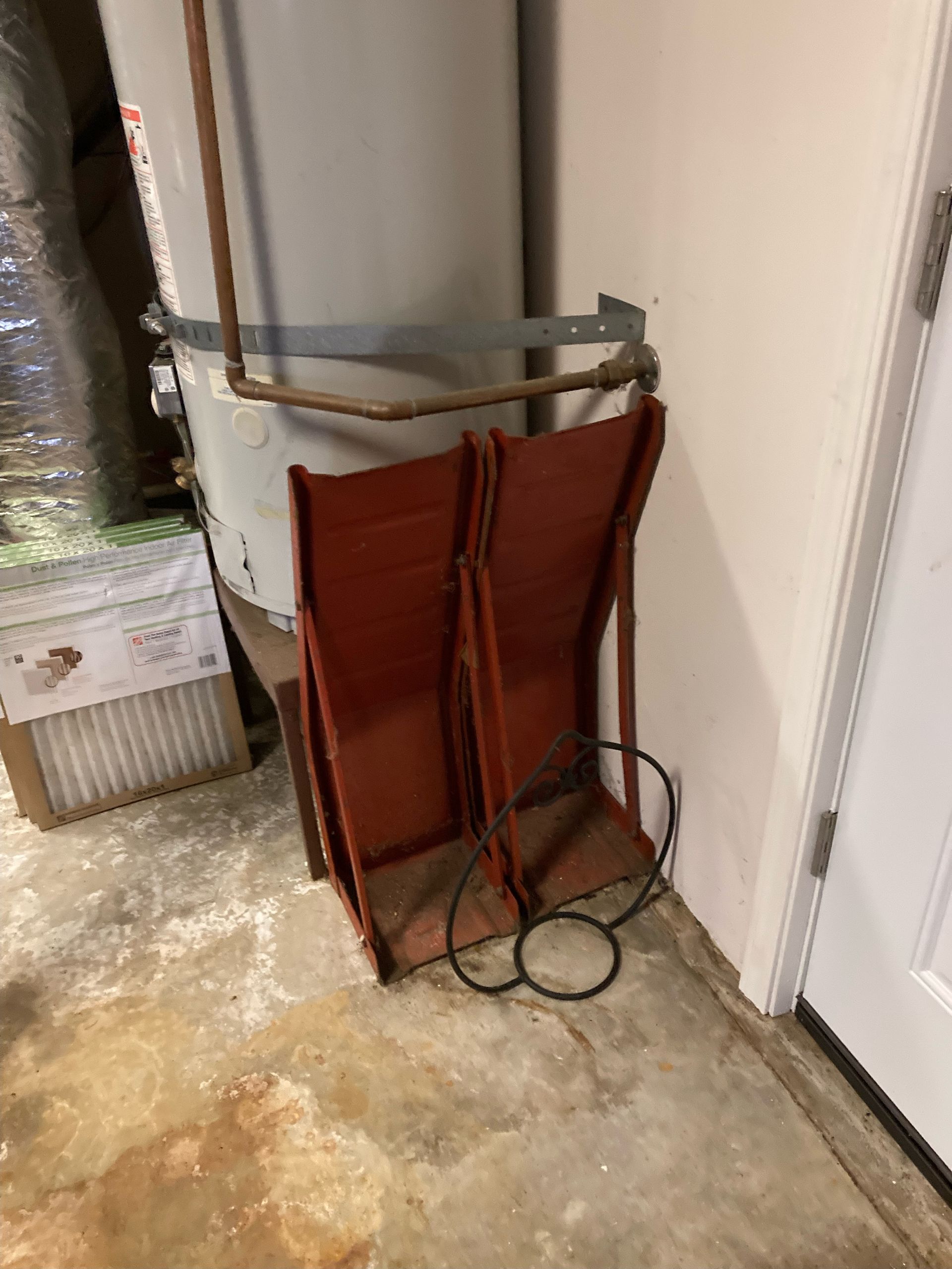 Two red metal chairs leaning against a water heater in a basement setting.