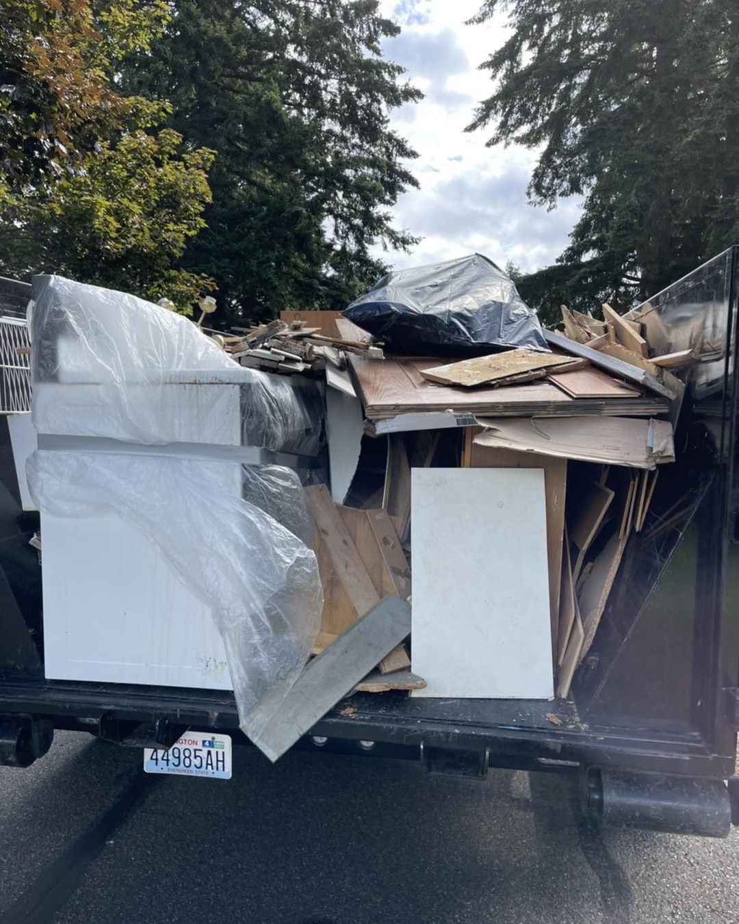 A truck bed overflowing with construction debris, including wood, cabinets, and plastic wrapping, outdoors.