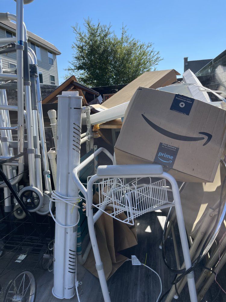 A cluttered pile of discarded items outdoors, including a ladder, box, and other white objects.