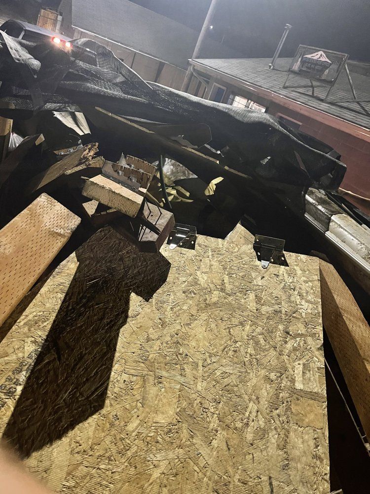 Pile of wood scraps, building materials, and a dark tarp against a building at night.