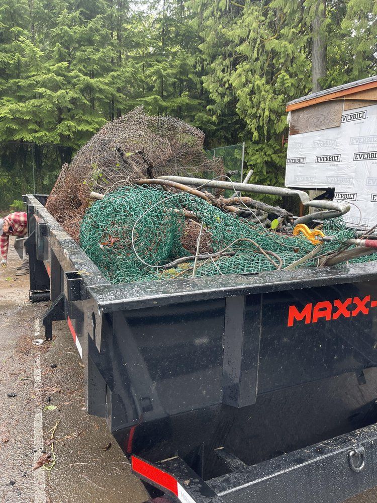 Black dumpster filled with debris including green netting, tree branches, and a person.