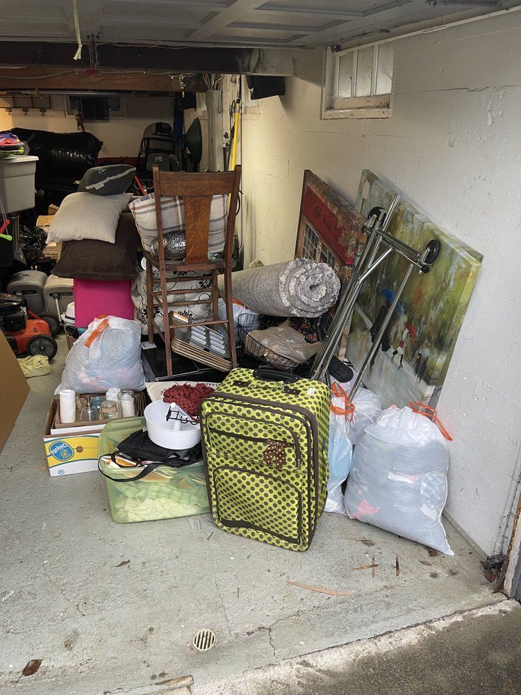 Cluttered basement: Chair, luggage, bags, rolled rug, art leaning against a wall, miscellaneous items.