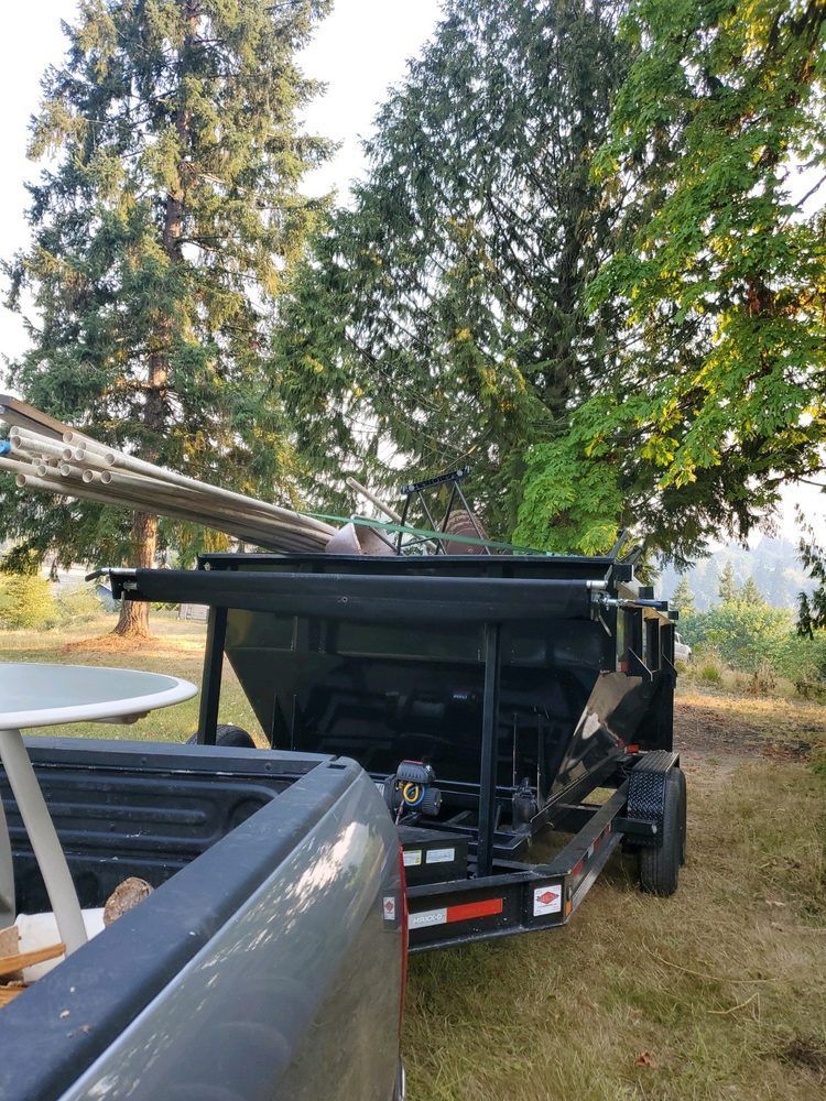 A trailer with a black bin, filled with debris, attached to a pickup truck outdoors.