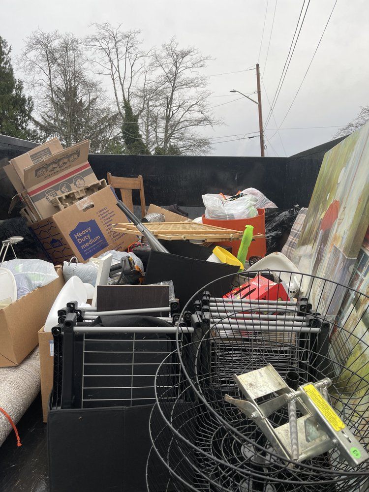 A truck bed filled with various household items, including boxes, furniture, and metal objects, against a cloudy sky.