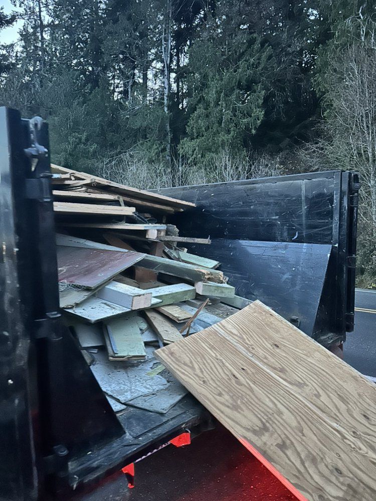 Dumpster overflowing with construction debris, including wood and siding, near a road.