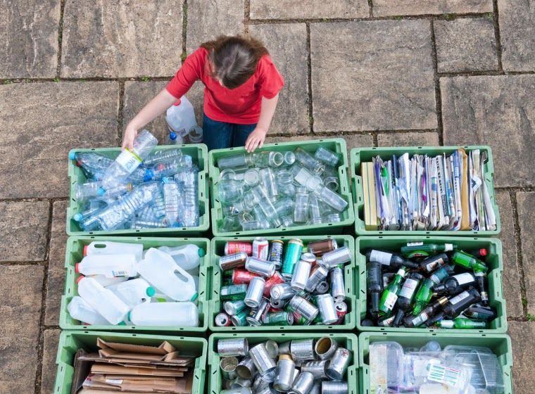 Person sorting recycling into bins of plastic bottles, glass, paper, and cans.