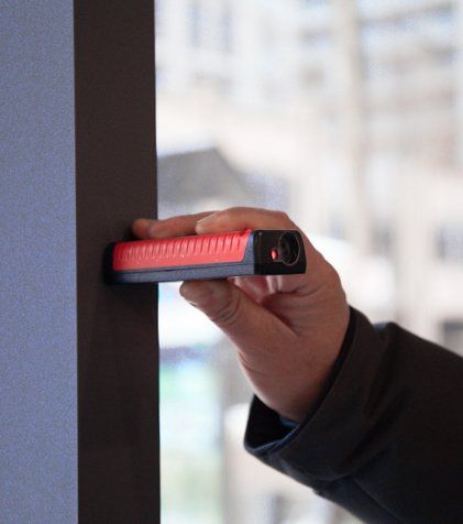 A person is measuring a wall with a red and black device