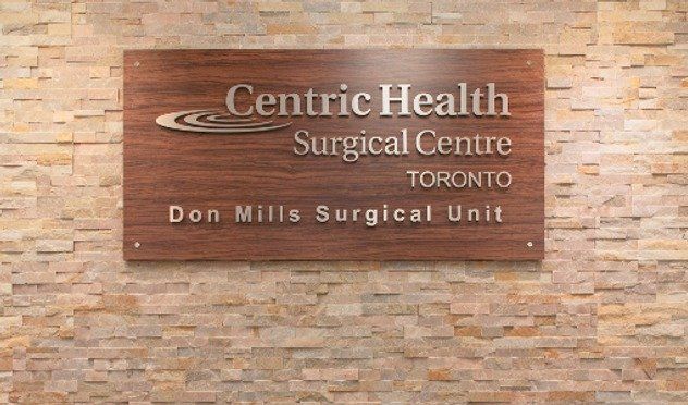 A wooden sign on a brick wall says centric health surgical centre toronto don mills surgical unit