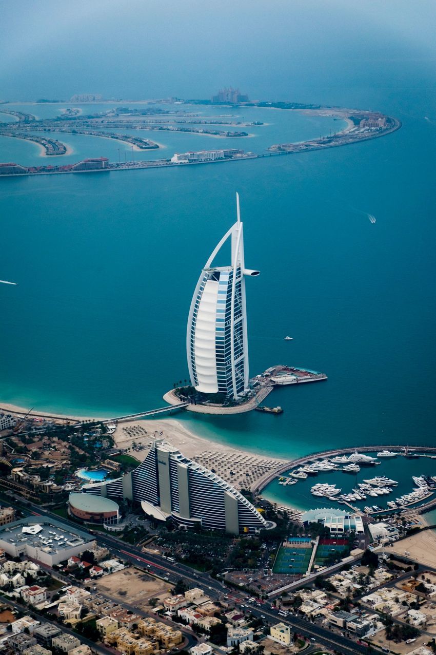 An aerial view of a city with a sailboat in the middle of the ocean.