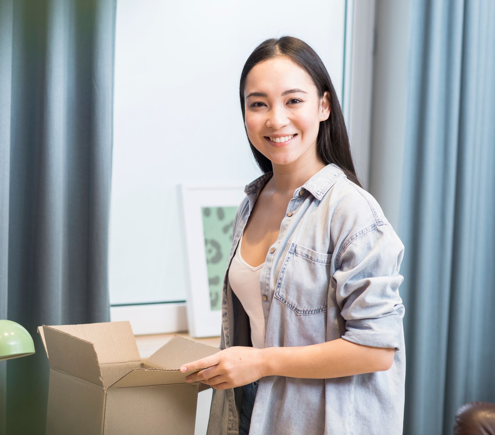 A woman is smiling while holding a cardboard box in a living room.