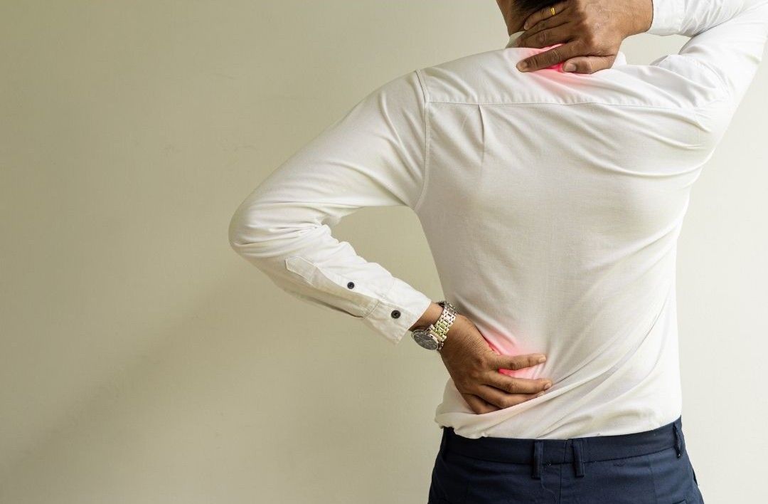 A person in a white button-down shirt holding their lower back and neck, showing signs of pain or discomfort.