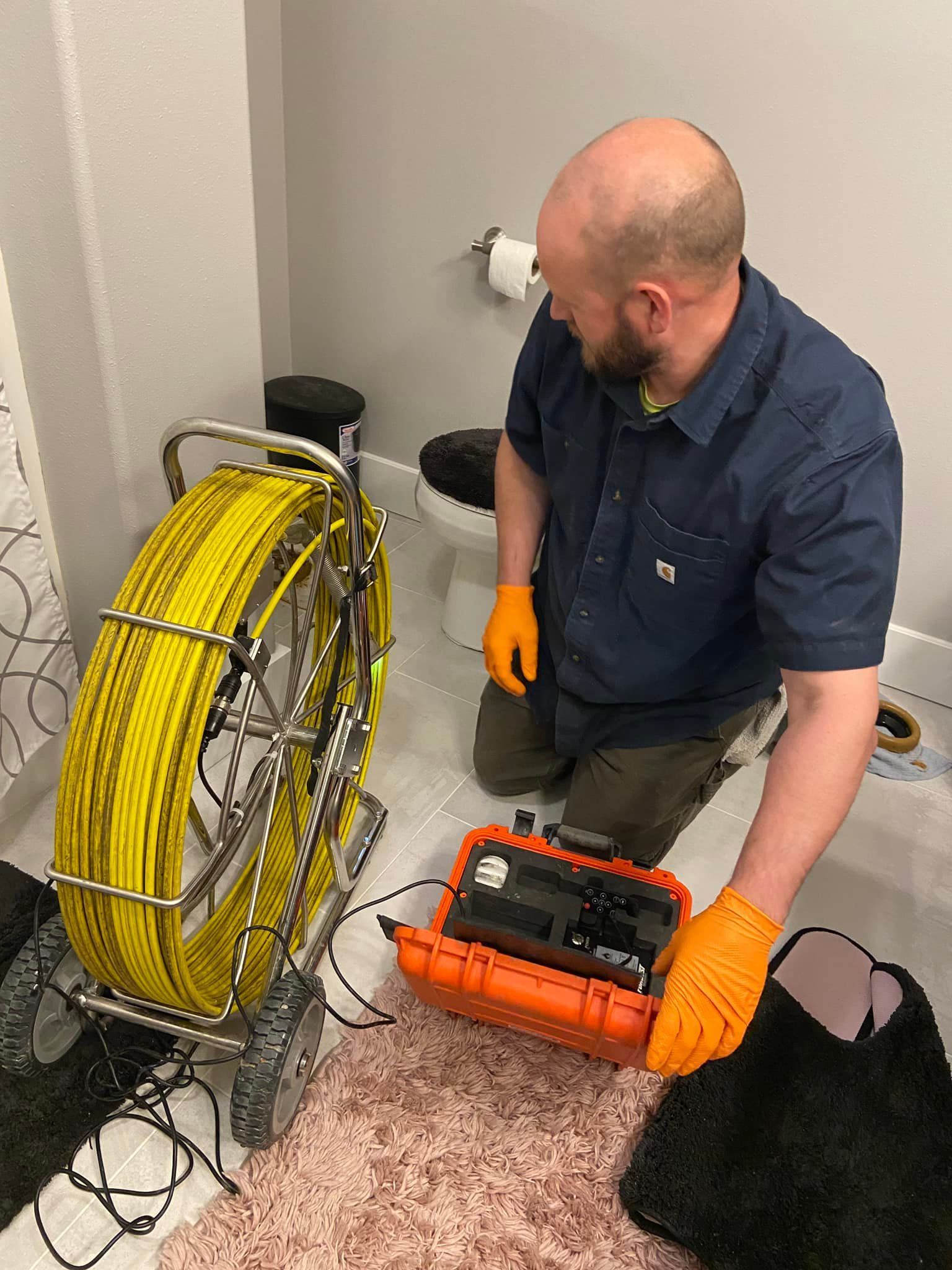 A man is kneeling down in a bathroom next to a drain camera.