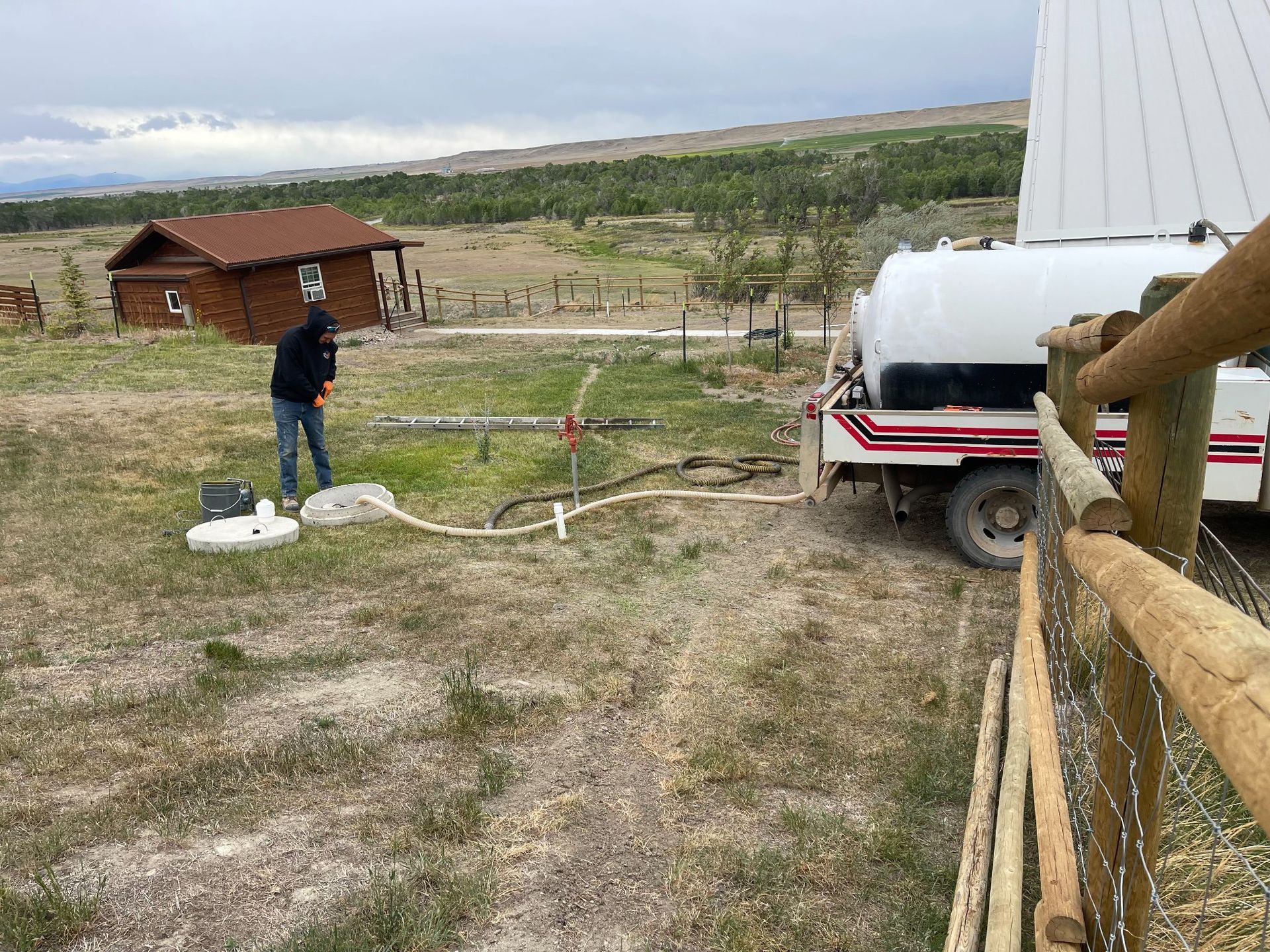 A man is standing next to a tanker truck in a field.