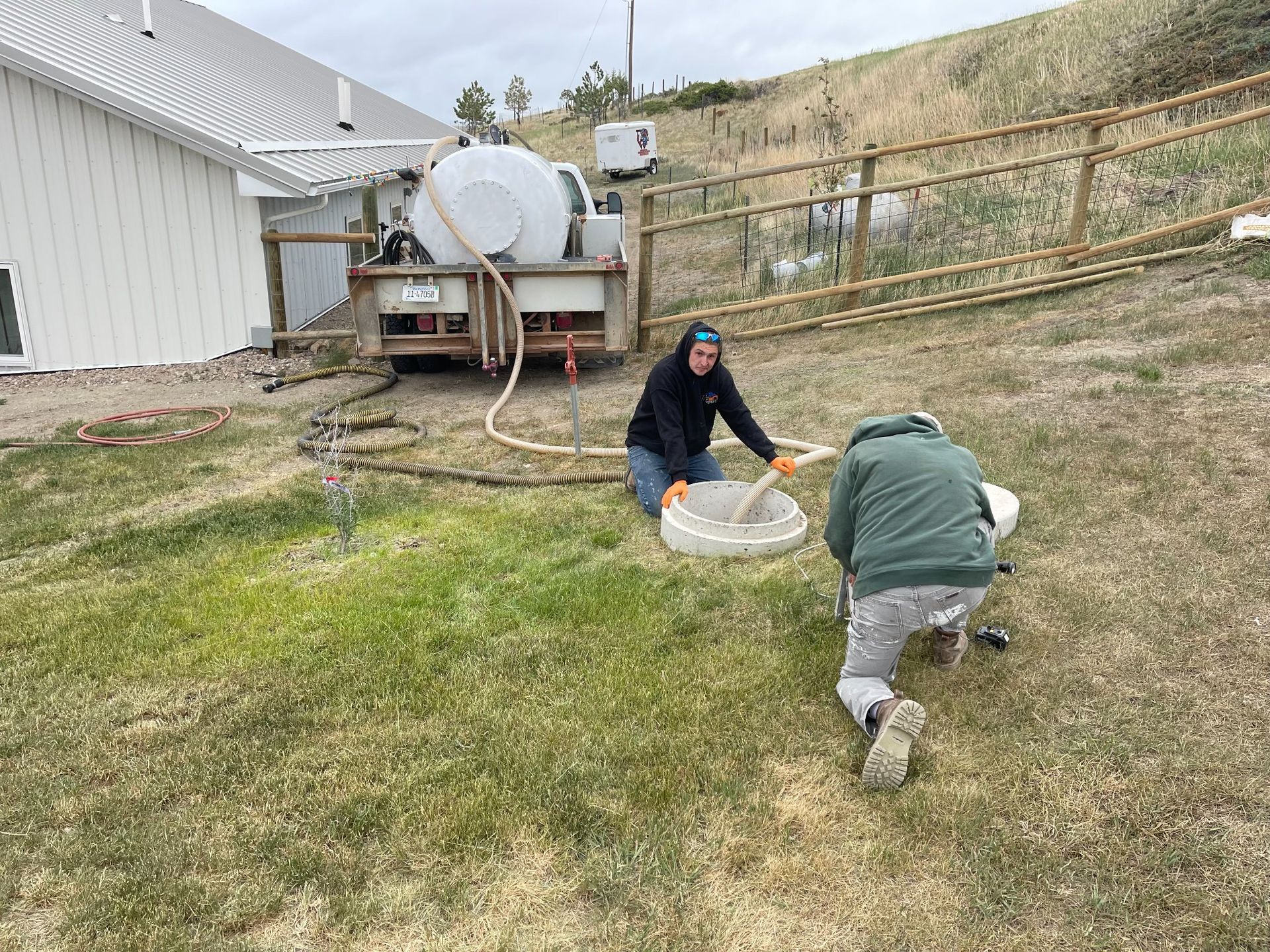 Two men are working on a septic tank in a backyard.