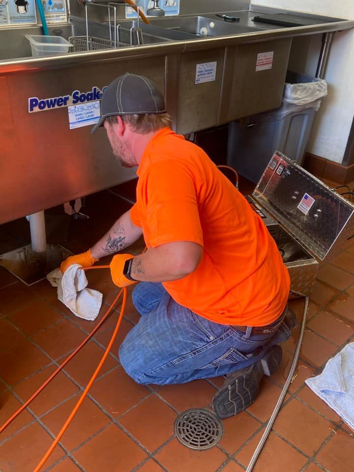 A man is kneeling down under a sink in a kitchen.
