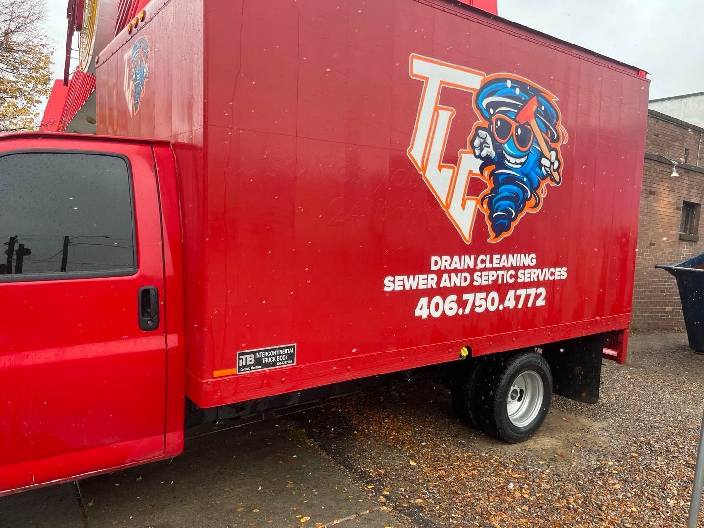 A red drain cleaning truck is parked in front of a building.