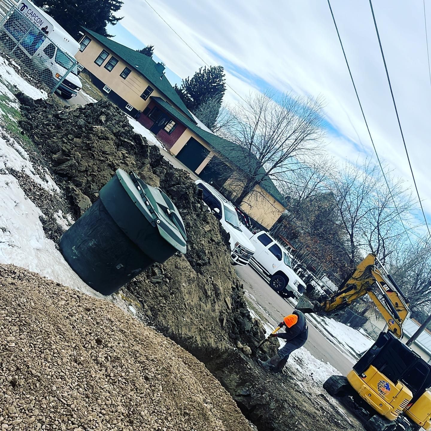 A man is digging in the dirt next to a yellow excavator.