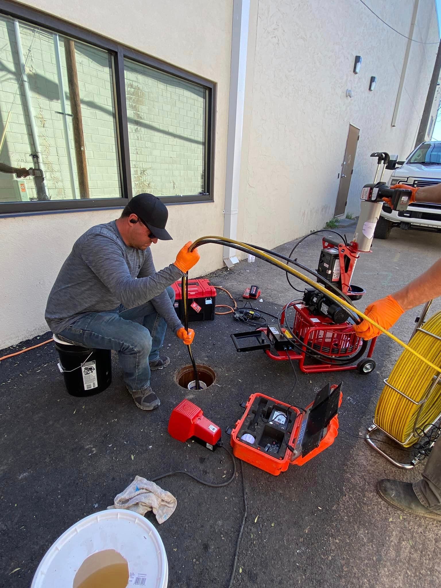 A man is kneeling down on the ground using a hose to drain a drain.
