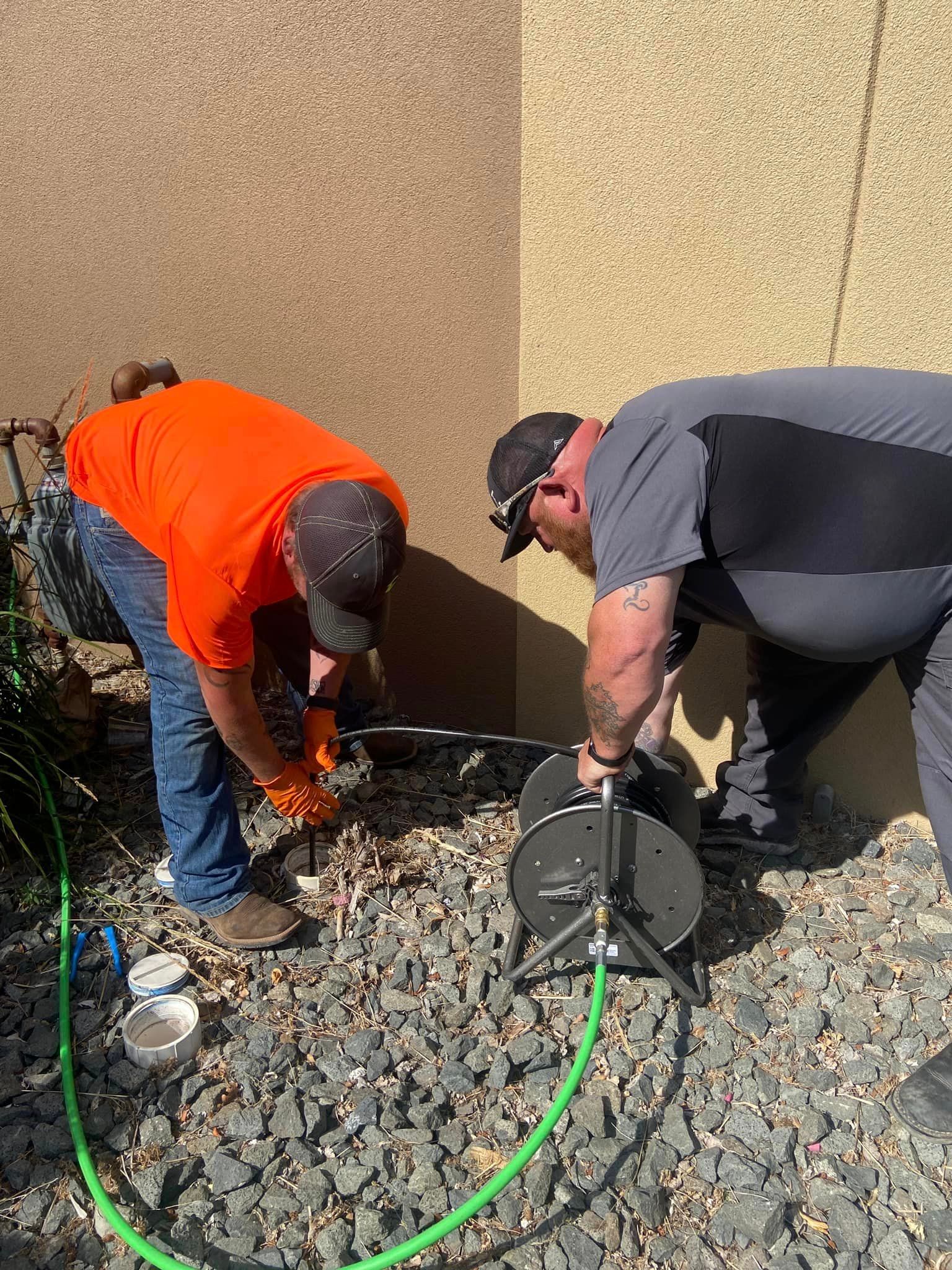 Two men are working on a pipe outside of a building.