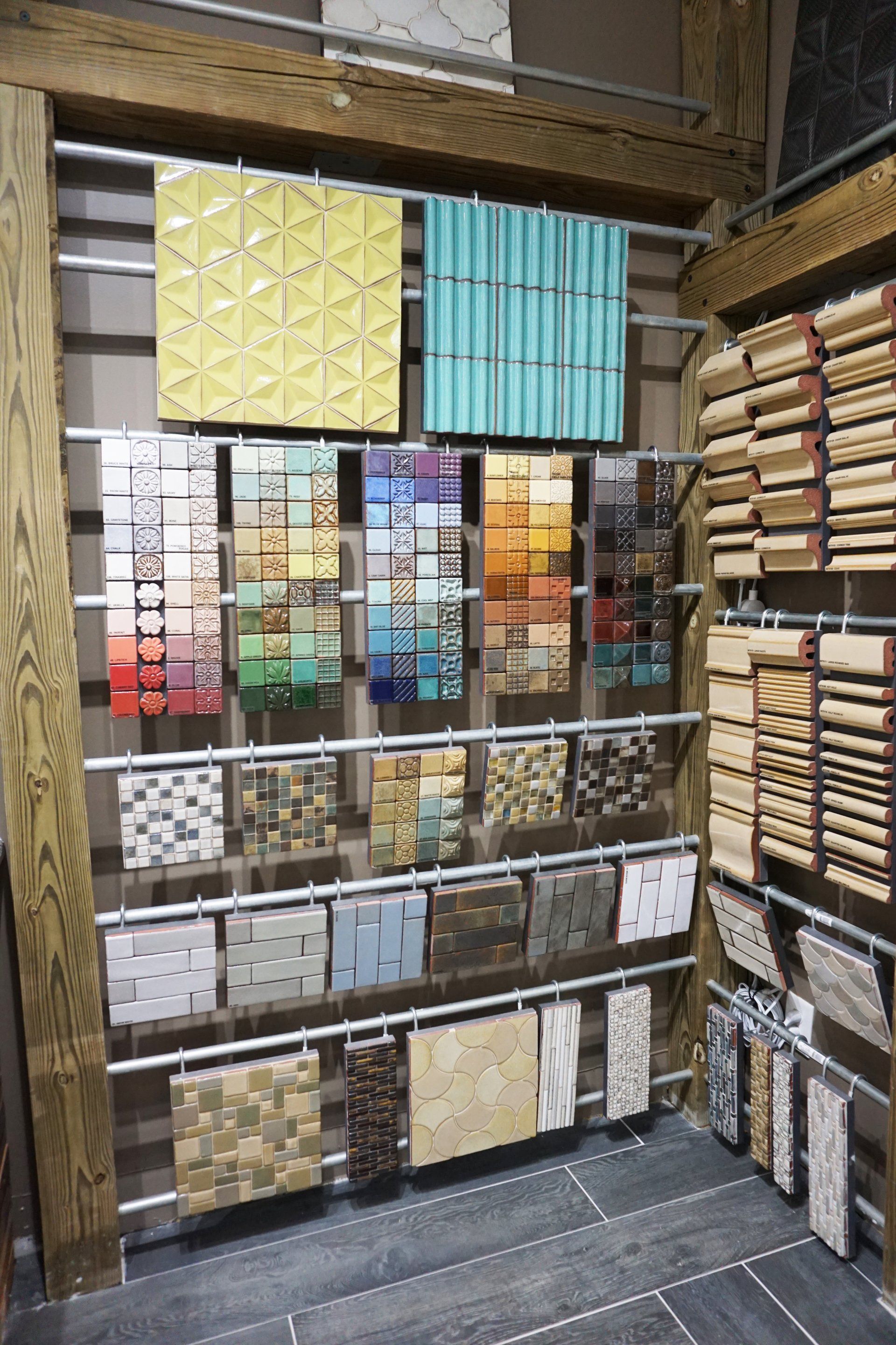 Tile samples displayed on a metal rack in a showroom, featuring various colors, textures, and patterns.