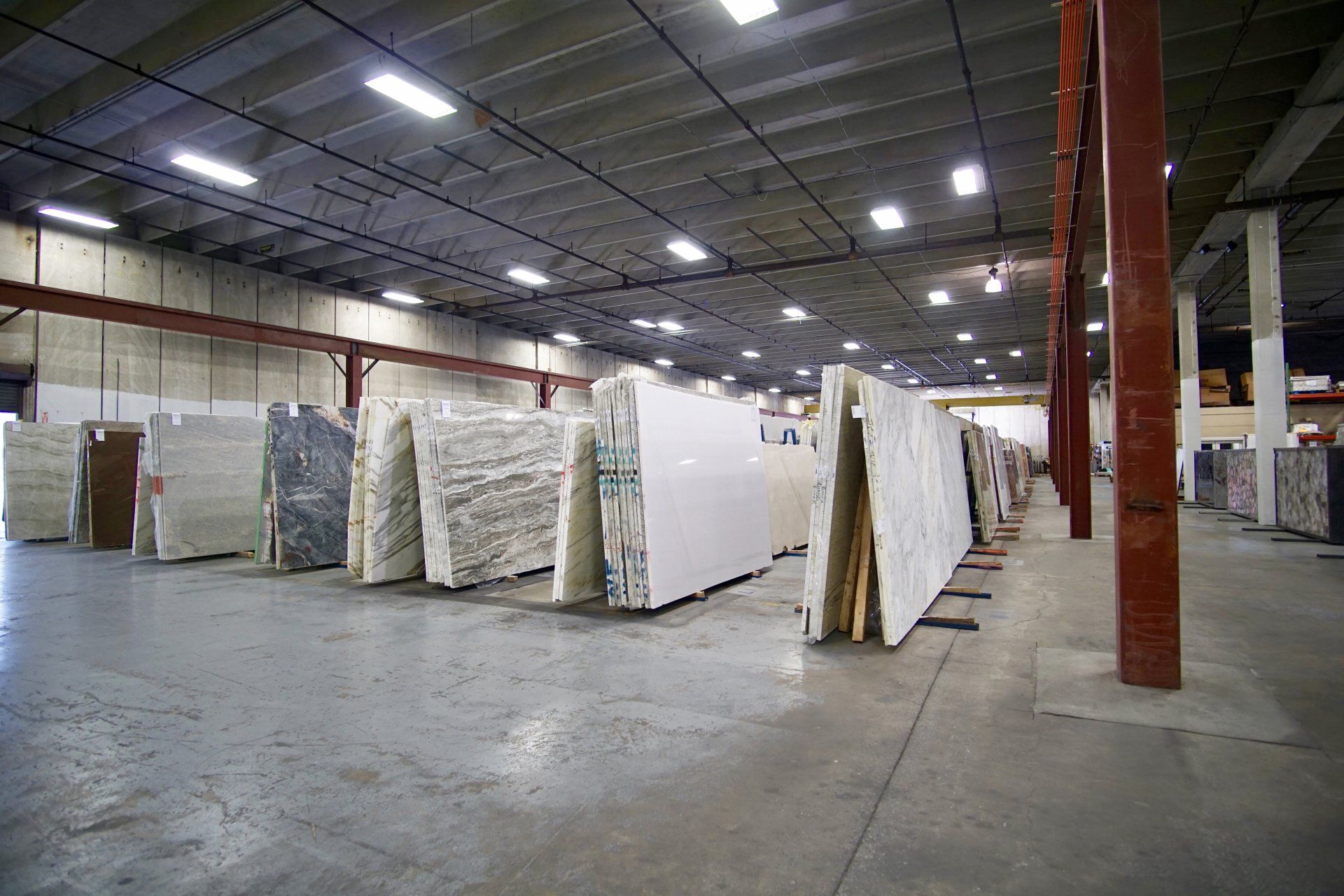 Rows of marble slabs in a warehouse setting, with a concrete floor and overhead lighting.
