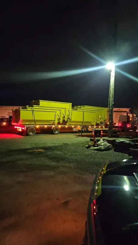 Yellow dump truck on a trailer, parked at night under a bright light.