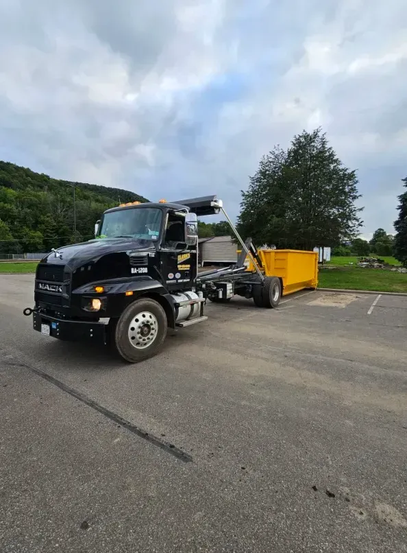 Black Mack truck with yellow dumpster, parked on pavement.
