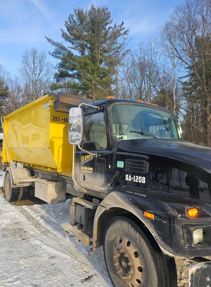 A black dump truck with a bright yellow container parked outdoors in a snowy landscape.