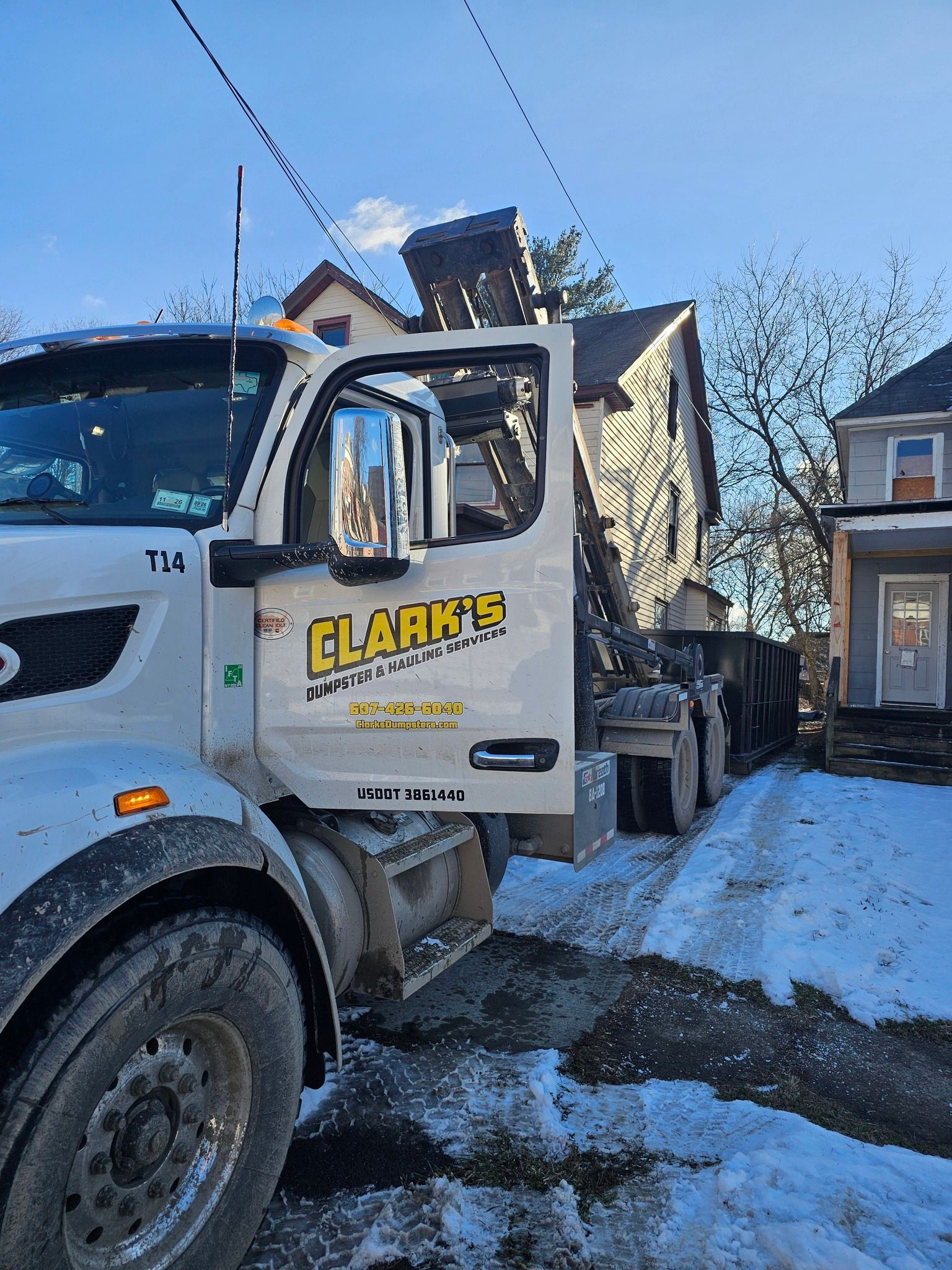 A white Clark's construction truck parked on a snowy, residential street in front of a house.