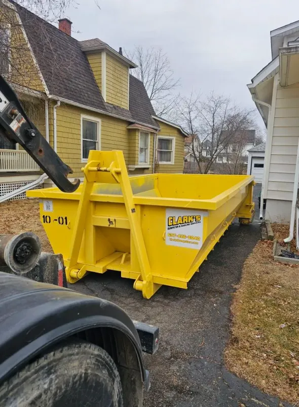A yellow dumpster is parked in front of a house.